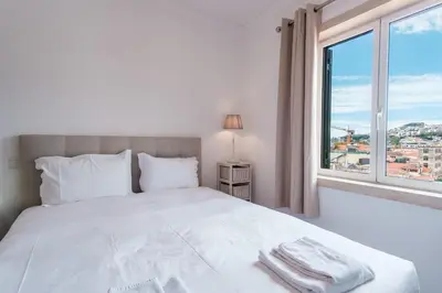 a bedroom with a white bed and a large window at GuestReady - Sao Tiago in Old Town in Funchal