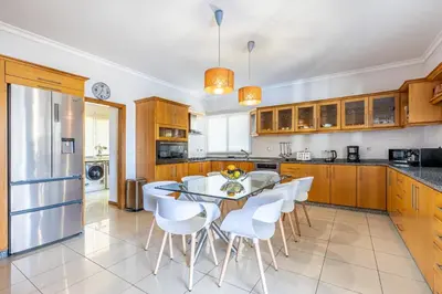 a large kitchen with a table and white chairs at Luxury villa with private heated pool, garden and views of the sea and mountains. in Arco da Calheta