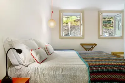 a bedroom with a bed with white sheets and two windows at Calheta Beach House T1 in Calheta