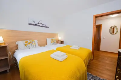 two beds in a room with yellow sheets and towels at Casa do Cantinho do Muro in São Vicente