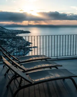 a group of chairs sitting on a balcony with the sunset at Peak A Boo Private Heated Pool and Private Parking in Câmara de Lobos