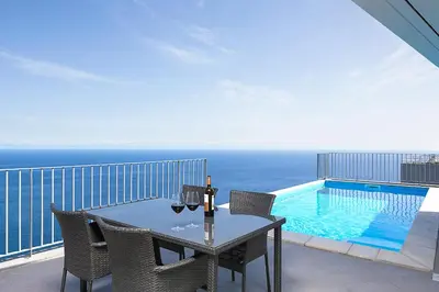 a table with wine glasses on a balcony with a pool at Peak A Boo Private Heated Pool and Private Parking in Câmara de Lobos