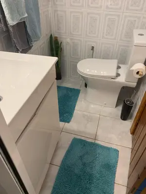 a bathroom with a white toilet and blue rugs at Waves Song - Cottage in Porto Moniz