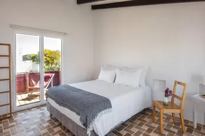 a bedroom with a bed and a table and a window at Sanderling beach & dune house in Carrapateira