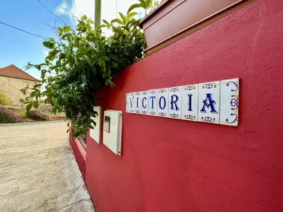 a sign on the side of a red wall with plants at Victoria Ocean View Room in Ponta do Pargo