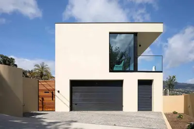 a white house with a black garage door at Villa Ohana in Estreito da Calheta