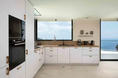 a kitchen with white cabinets and a large window at Villa Ohana in Estreito da Calheta